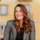Woman with long brown hair wearing a gray blazer against a blurred background